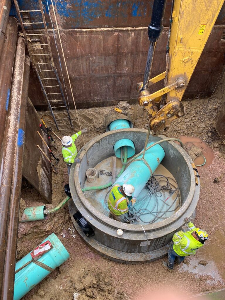A Mainline Contracting work site with heavy machinery, pipes and workers in a hole