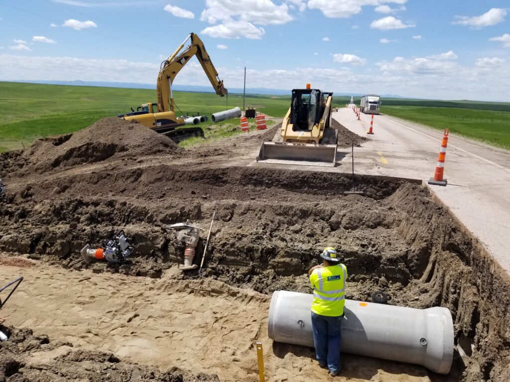 Heavy machinery surrounding a pipe project in a road at a Mainline Contracting site.